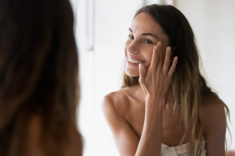 Frau schaut sich im Spiegel an: Auch die Gesichtspflege gehört zur Selfcare im Alltag